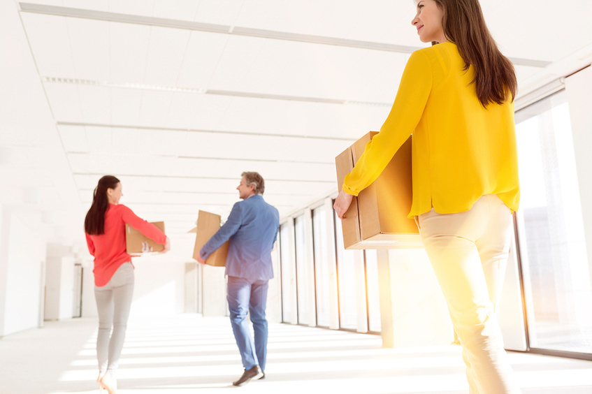 Three people walking through a hallway caring cardboard boxes.